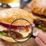 Someone examining burger with magnifying glass in a hand